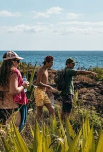 Trois personnes sur un sentier côtier, végétation et mer à l'arrière-plan.