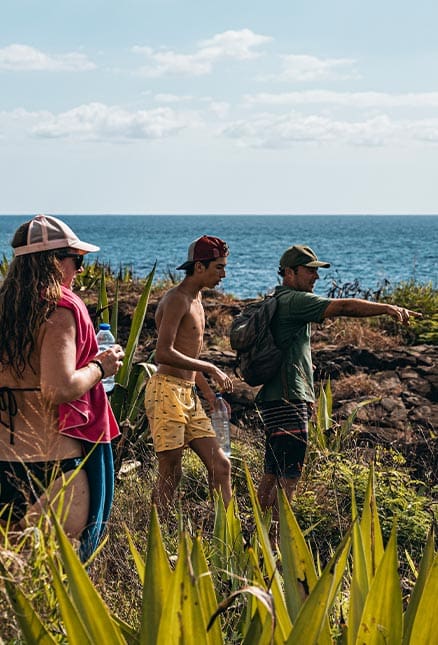 Trois personnes sur un sentier côtier, végétation et mer à l'arrière-plan.